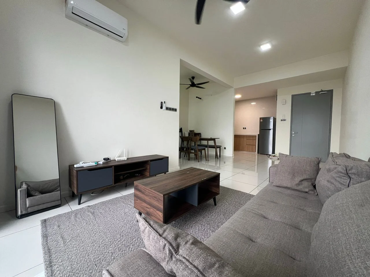 Living features: 3-seater fabric sofa in grey, coffee table, TV console, wall-mounted TV, area rug, floor-to-ceiling mirror, ceiling fan, recessed LED downlights, white painted walls, tile flooring, 1 wall-mounted split AC; style: modern. Dining features: dining table, 4 dining chairs, open layout to kitchen, white painted walls, tile flooring; style: modern.